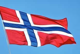 Eine Flagge Norwegens weht vor blauem Himmel im Wind.