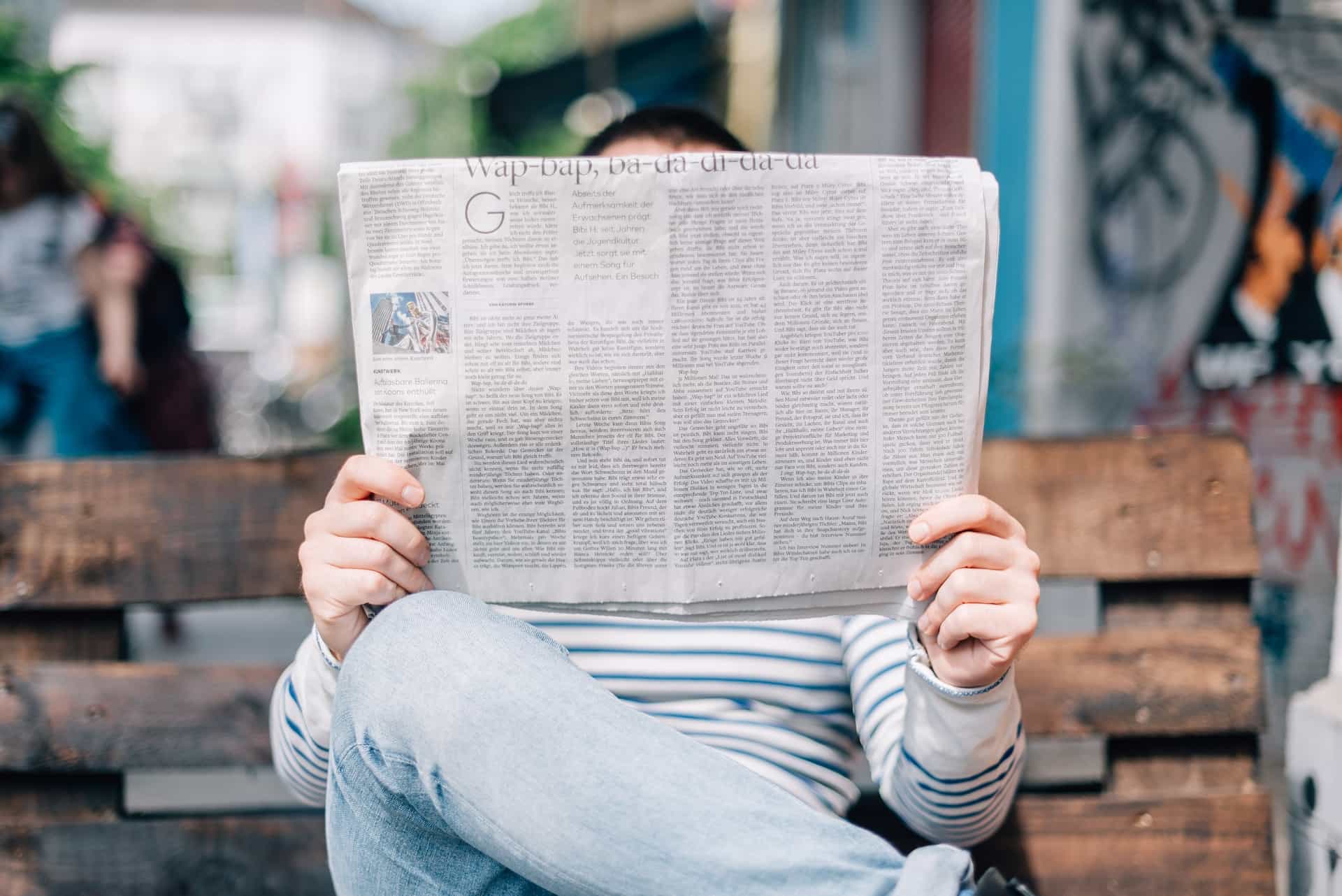 Eine Person liest eine Zeitung auf einer Bank.