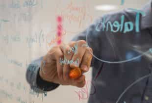 Eine Person schreibt auf ein Glas-Whiteboard.