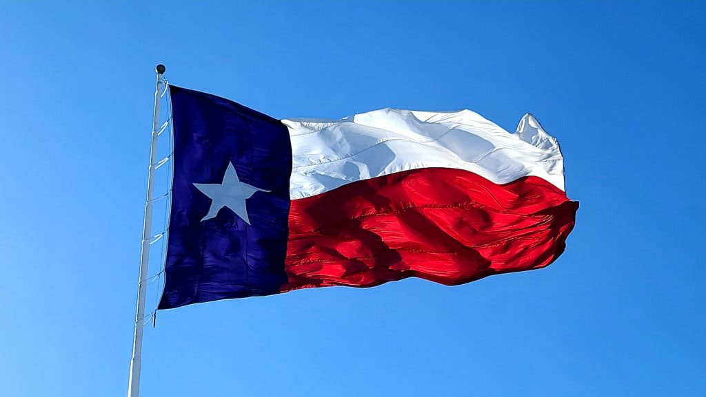 Eine Texas-Flagge am Mast weht bei blauem Himmel im Wind. 