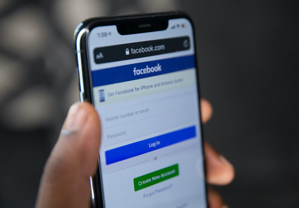 Eine Person hält ein Smartphone mit dem Facebook-Login auf dem Display.