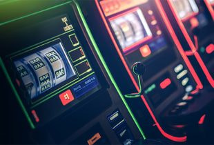 Eine Reihe von Spielautomaten mit blinkenden Lichtern und einem schwach beleuchteten Spielbereich im Hintergrund.