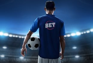 Fußballspieler mit Trikot, das Werbung für einen Wettanbieter zeigt, während ein Stadion im Hintergrund sichtbar ist.