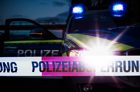 Ein Polizeiauto mit eingeschaltetem Blaulicht steht nachts vor einem abgesperrten Bereich, der mit Flatterband markiert ist.