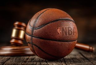 Ein Basketball auf einem Hartholz-Gerichtsboden, auf dem ein Richterhammer liegt.
