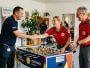 Zwei Vertreter des Deutschen Roten Kreuzes nehmen freudig einen neuen Kickertisch von einem Mitarbeiter der Merkur Group entgegen.