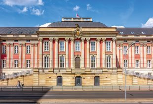 Das historische Gebäude des Landtags in Brandenburg bei Tag. Vor dem Gebäude wehen mehrere Flaggen im Wind.